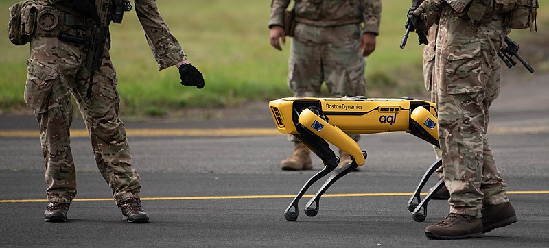 A Boston Dynamics SPOT robot is walking between air force officers in camouflage.